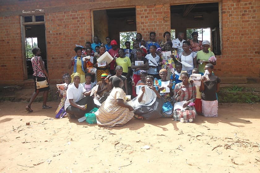 A large community gathering seated outside a building during a Kiyunga Social Service Centre village dialogue.
