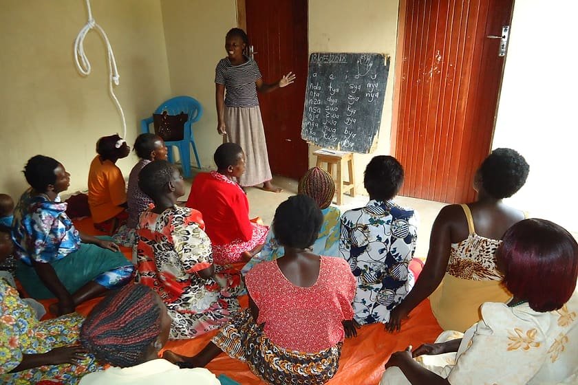 Women seated in a circle listening to a facilitator during a Kiyunga Social Service Centre community discussion.