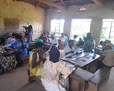 Women and young people seated at desks working through printed materials during a training session.