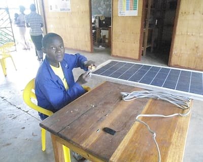 A young woman working with a solar panel and cabling at a table.