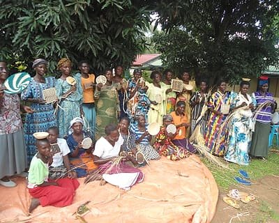 A women's group seated outdoors weaving mats and baskets together.